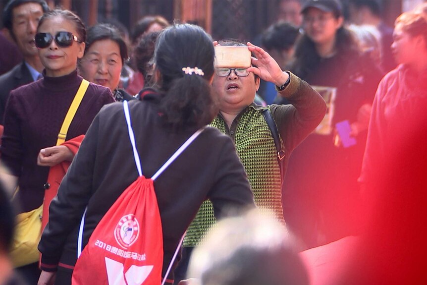 a man holds a phone up to capture footage as a crowd of people surround him