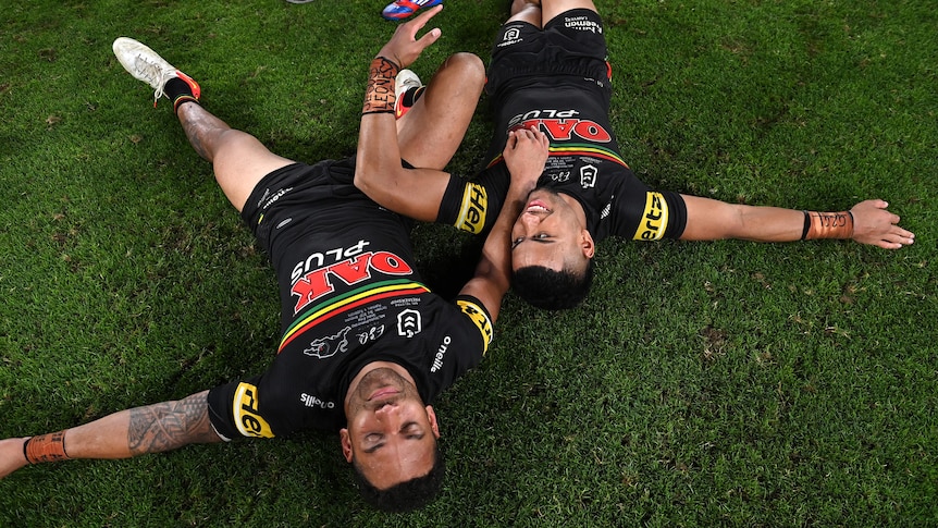 Penrith Panthers players Apisai Koroisau and Stephen Crichton lie on the grass field after the 2021 NRL grand final.