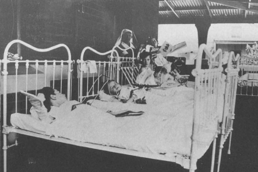 Children sleeping in beds are lined up on the verandah in a black-and-white photo.