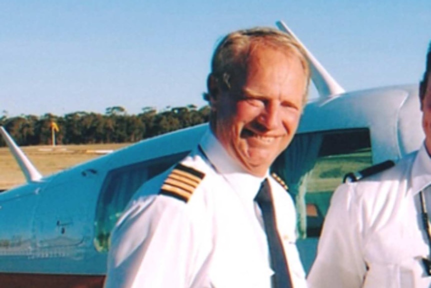 Chris Gobel smiles as he stands in front of an aircraft in a pilot's uniform.