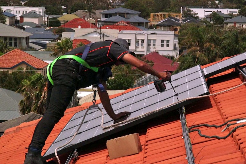 A workman attaches a solar panel to a roof.