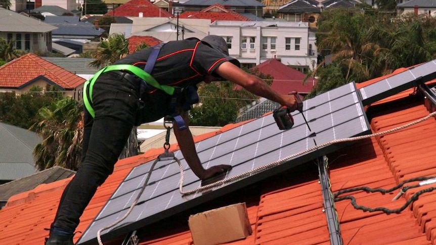 A workman attaches a solar panel to a roof.