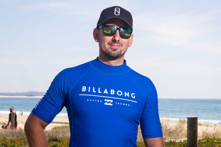 Matt Formston wears a blue rash vest, hat and sunglasses at the beach.