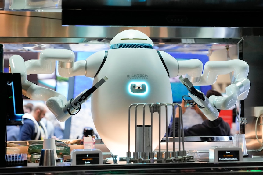 A medium shot of a robot barista standing behind a counter and holding up its arms slightly.