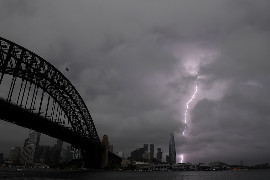 A purple lighting bolt strikes through stormy clouds next to the Sydney Habour Bridge.