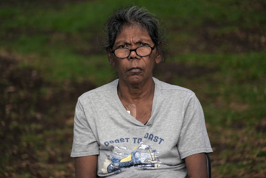 An Aboriginal woman with a bandage on her chest stares at the camera. 