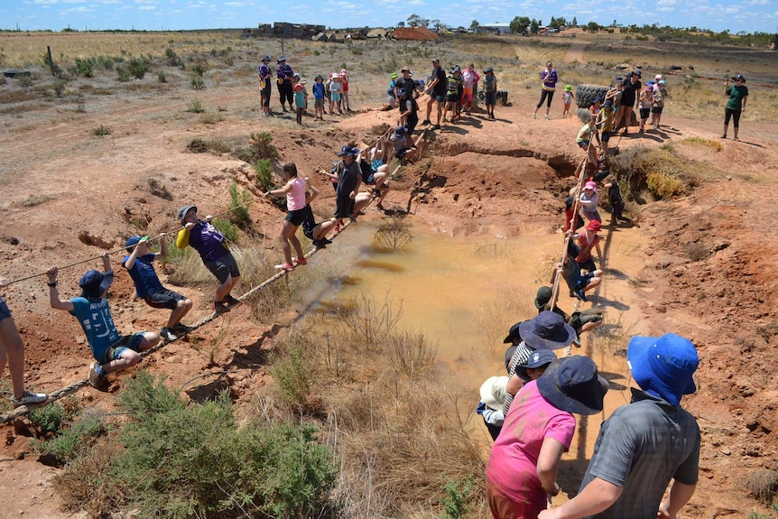 Children grip ropes as they cross above a mud crossing.