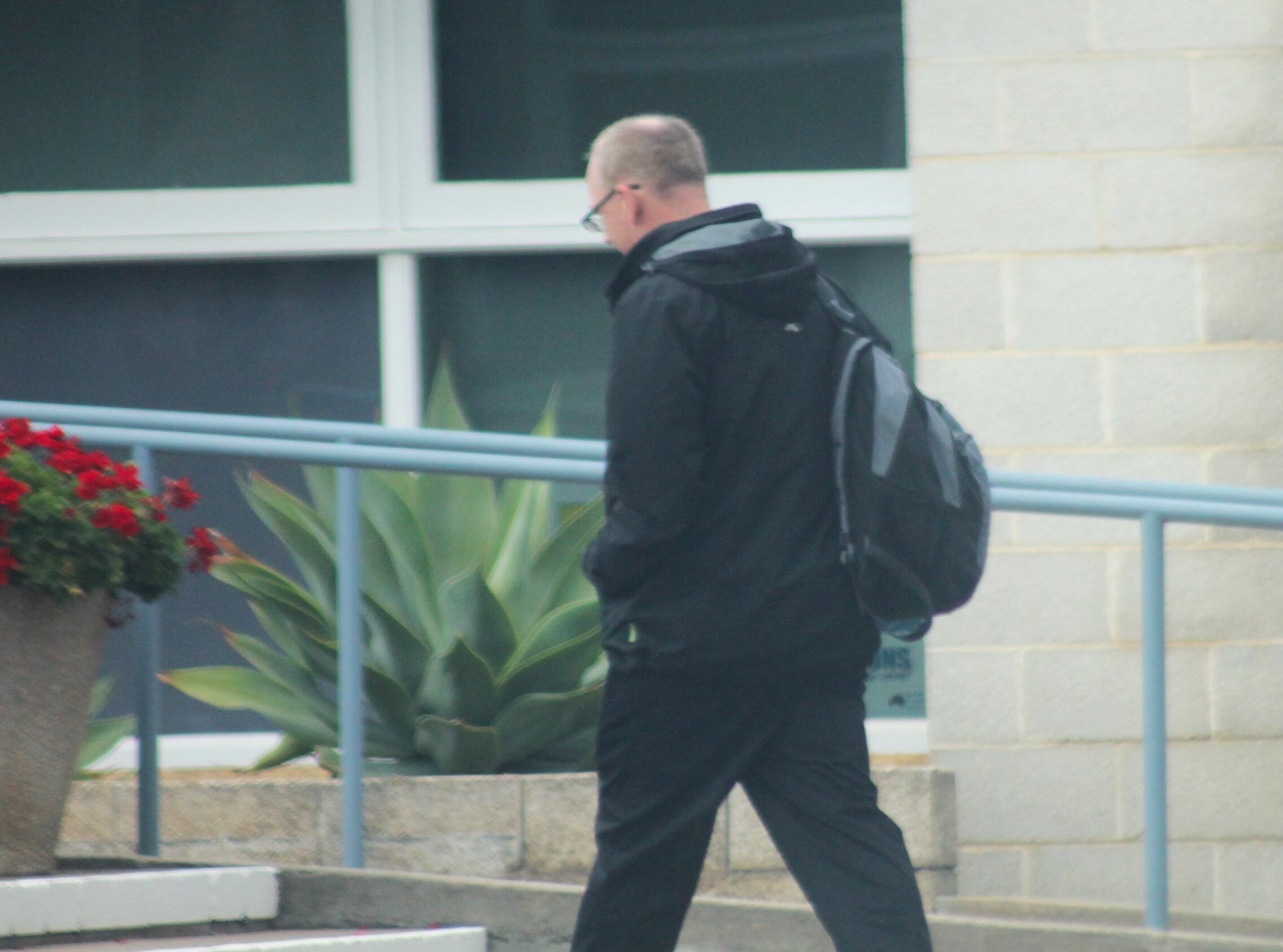 Man wearing black jacket walking with back turned to camera, holding a bakcpack on one shoulder