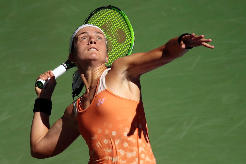 A female tennis player looks up at the ball with her racquet behind her in preparation to serve