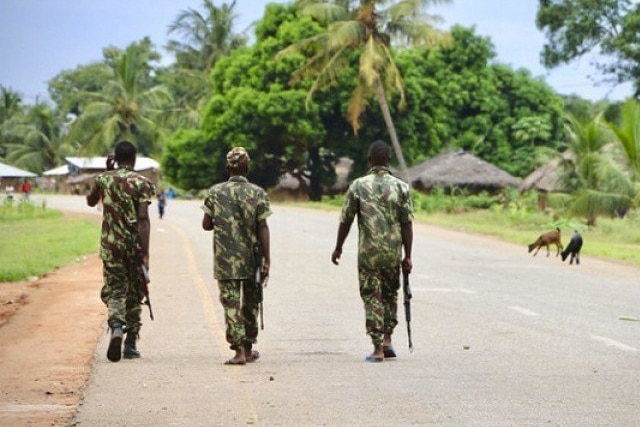 Three African soldiers walk down the middle of a quiet street in tropical setting.