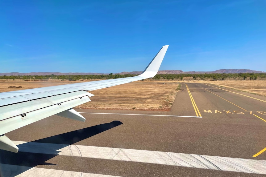 The wing of an airplane next to a runway with Kununurra landscapes in the distance
