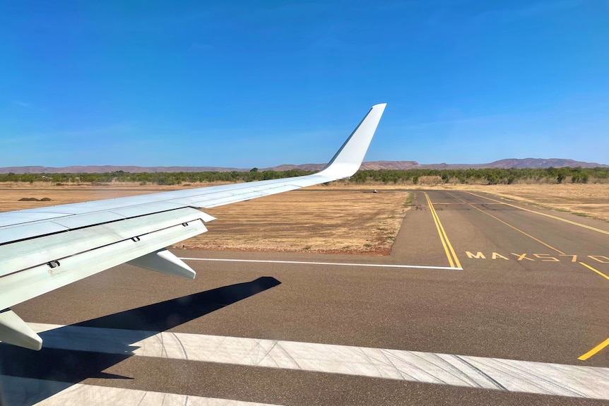 A plane's wing next to a runway with Kununurra scenery in distance