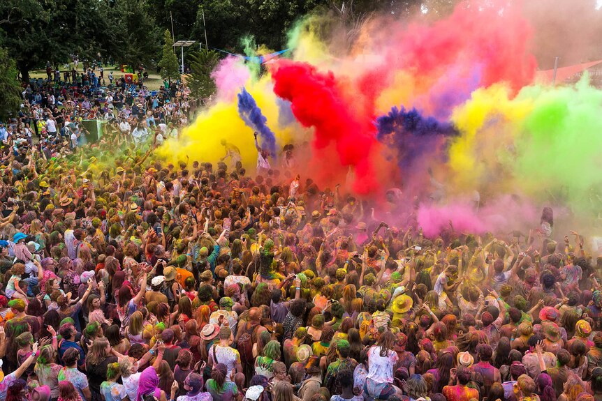 A crowd of people are covered with explosions of colourful powder at a festival