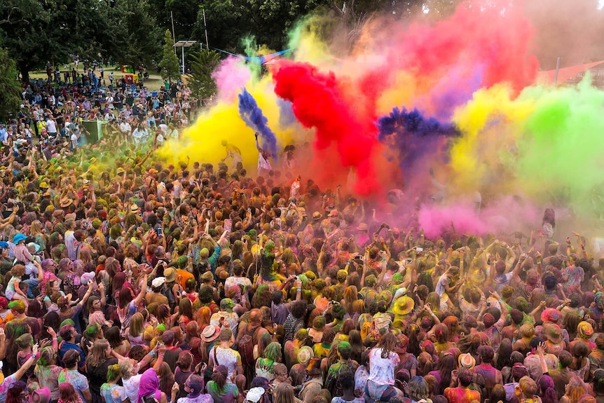 A crowd of people are covered with explosions of colourful powder at a festival