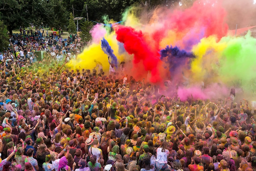 A crowd of people is covered with explosions of colourful powder at a festival.