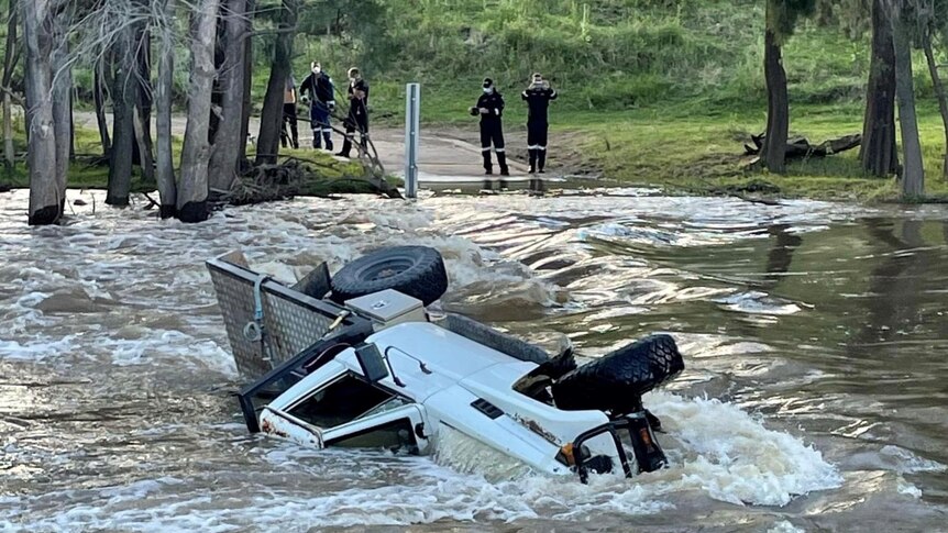An overturned ute in the middle of a fast flowing river. 