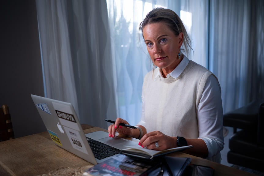 A woman sits behind a laptop at a desk.