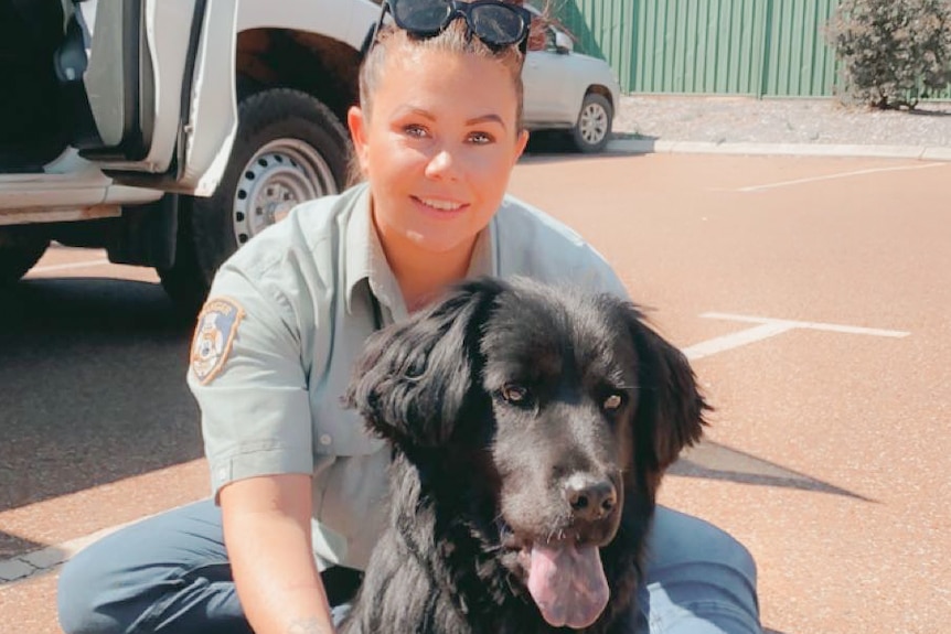 A shire ranger woman, crouched down smile with a black spaniel dog.