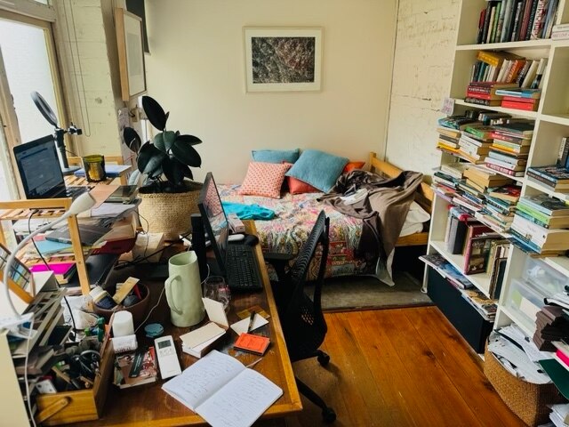 Author Charlotte Wood shares her home office, with a cluttered desk, a full bookshelf and a bed with multiple cushions for naps