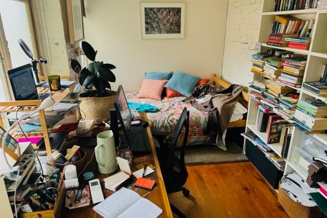 Author Charlotte Wood shares her home office, with a cluttered desk, a full bookshelf and a bed with multiple cushions for naps