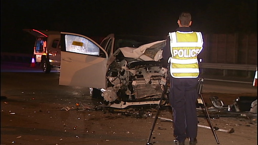 Police stand in front of a car smashed up from an accident.