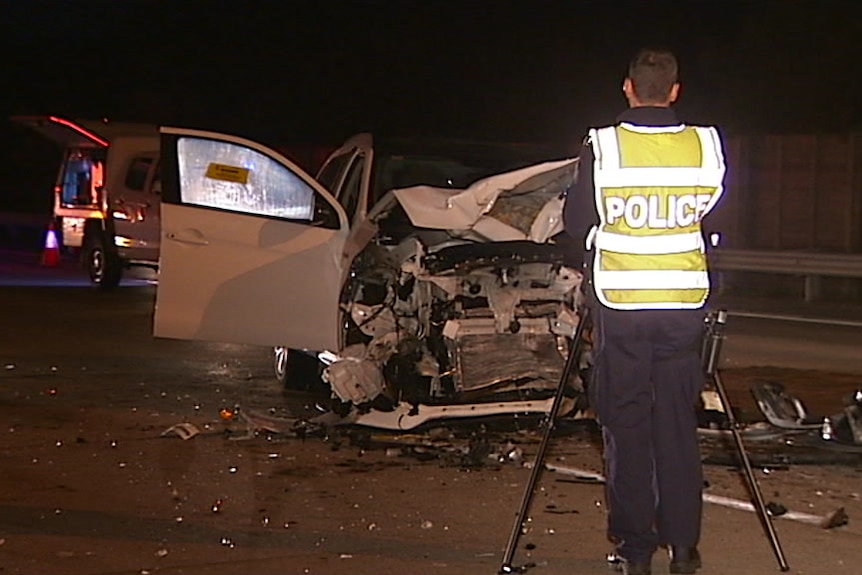 Police stand in front of a car smashed up from an accident.