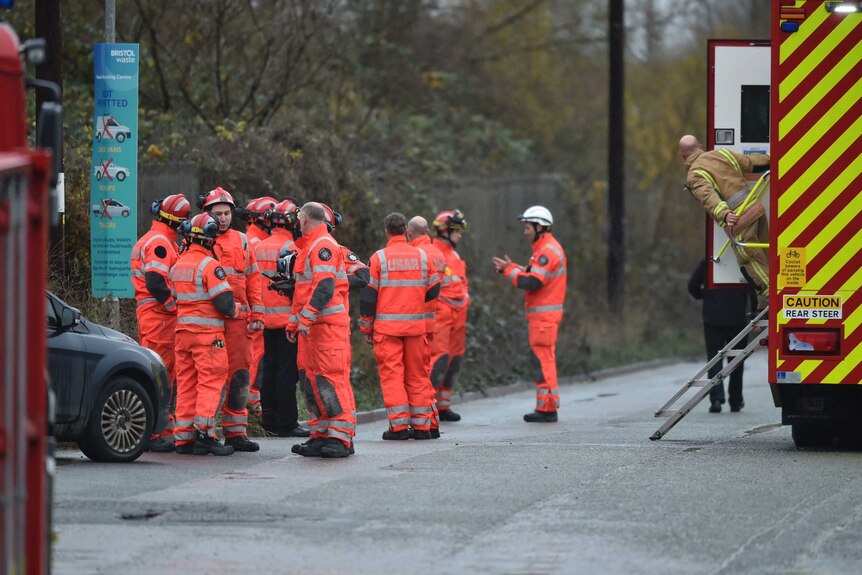 British emergency service workers in bright orange uniforms gather on a road