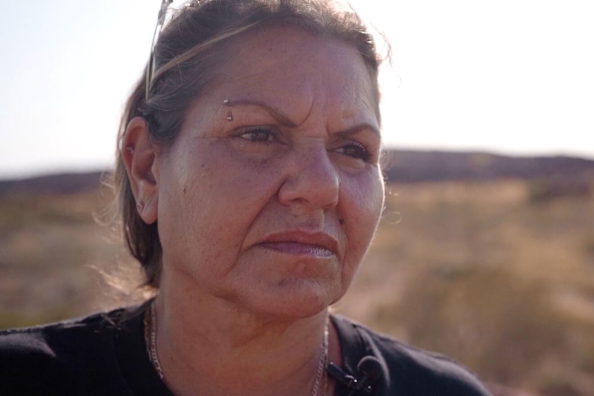 A woman looks sad while standing in the outback.