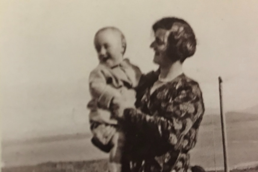 Black and white photograph of a smiling baby held by a woman