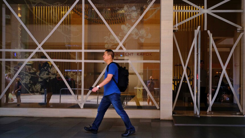 Wide shot of a man walking past taped up windows.