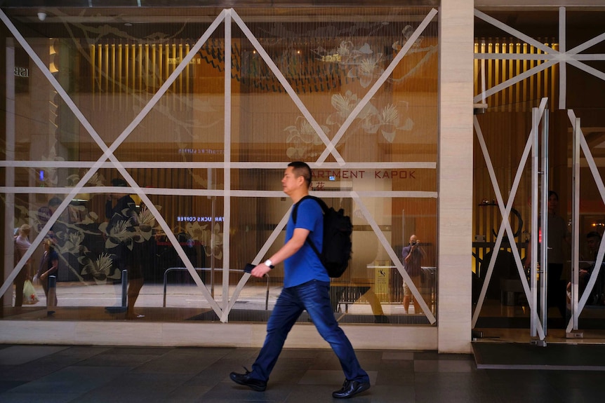 Wide shot of a man walking past taped up windows.