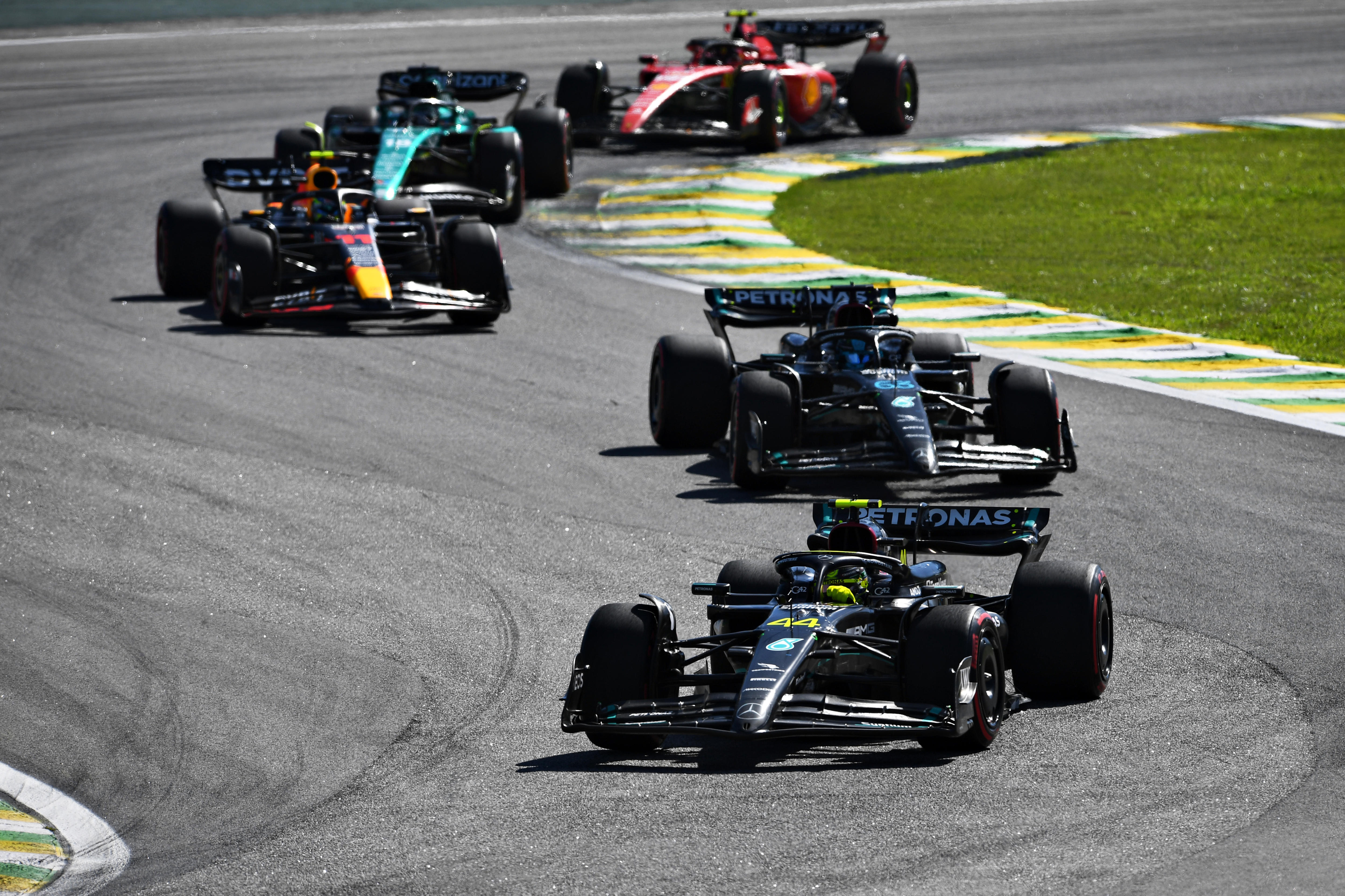 Two black F1 cars leading three more cars, going through a chicane on track