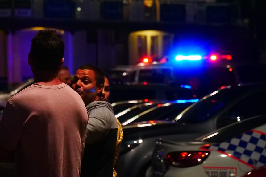 Onlookers at the beach near police cars flashing emergency lights