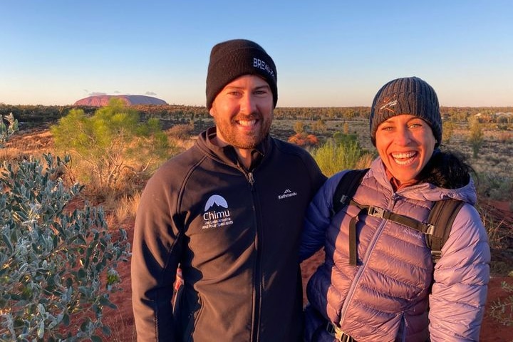 A couple pose for a picture with Uluru in the background.