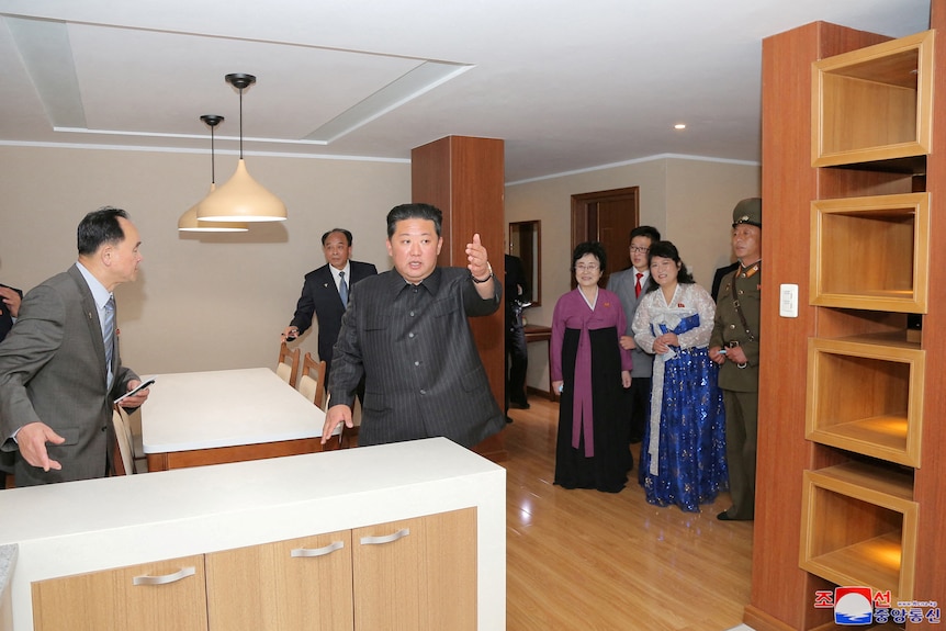 김정은 위원장이 평양의 새 아파트를 견학하는 군중들에게 팔을 내밀고 있다.