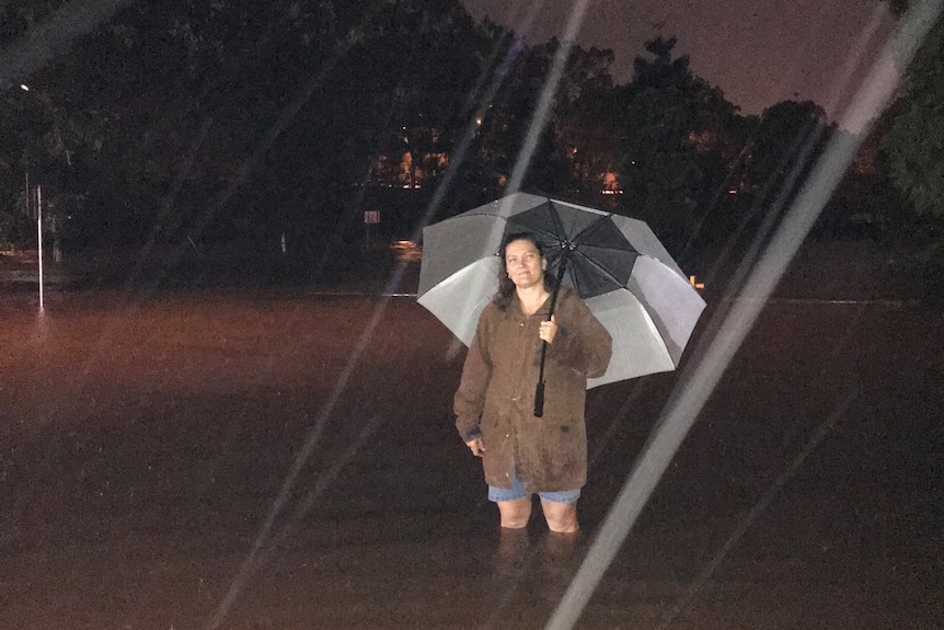 A woman standing in floodwater, holding an umbrella.