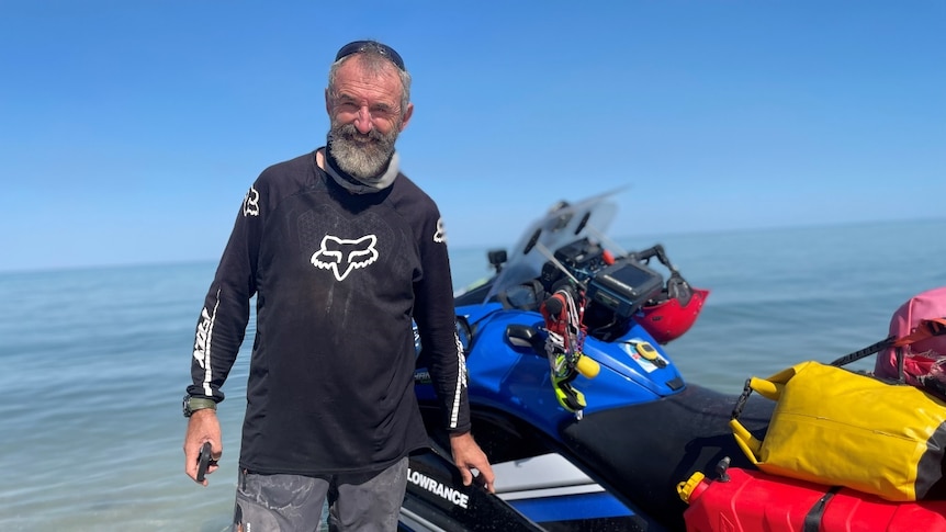 A man standing next to a jetski at a beach