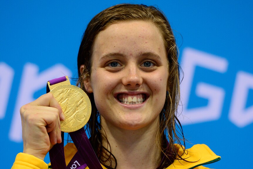 Swimmer Ellie Cole holds a Paralympic gold medal next to her face and smiles