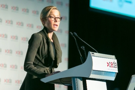 Emma Roberts speaks at a CEDA event on stage behind a lectern.