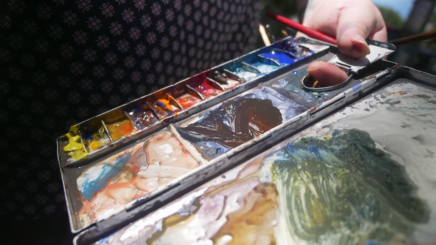 Mixed watercolour paints on a palette, being held by painter.