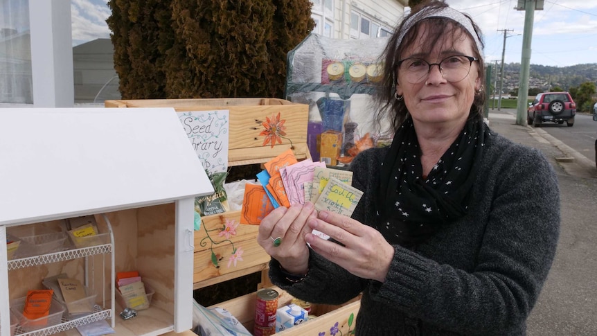 Woman holding home-made packets of seeds up while standing in front of a street seed library