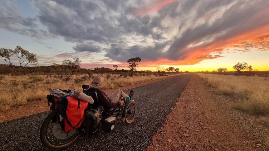 A man on a tricycle looks along the road to a sunset