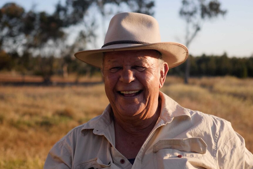 Aboriginal elder Kevin Barron wearing a stock hat and sitting in a paddock in the late afternoon sun.