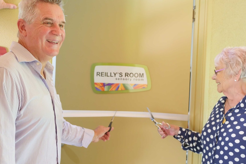 a man and woman holding scissors cut the ribbon to a room labelled 'Reilly's Room'