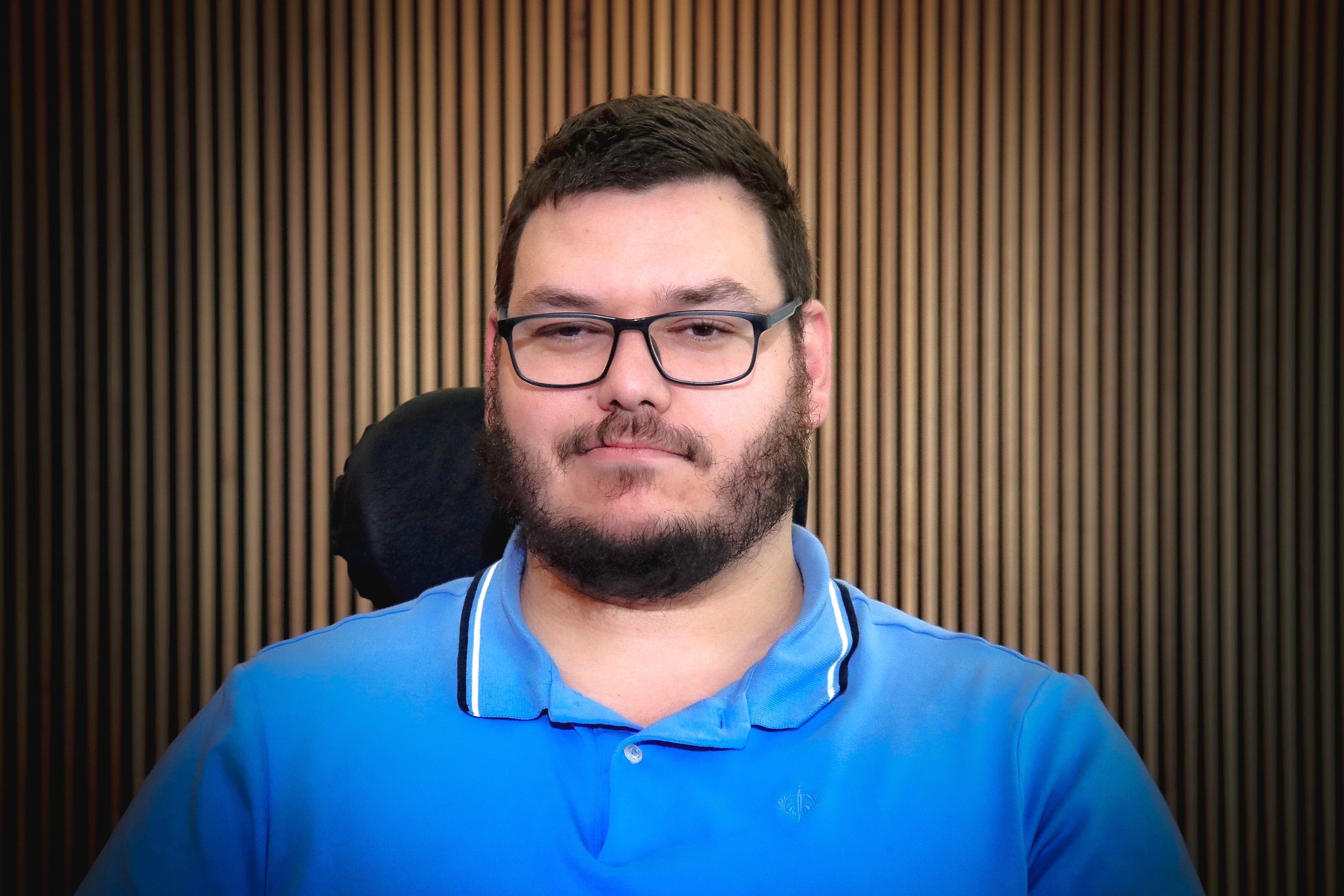 A man with glasses wearing a blue shirt in a wheelchair