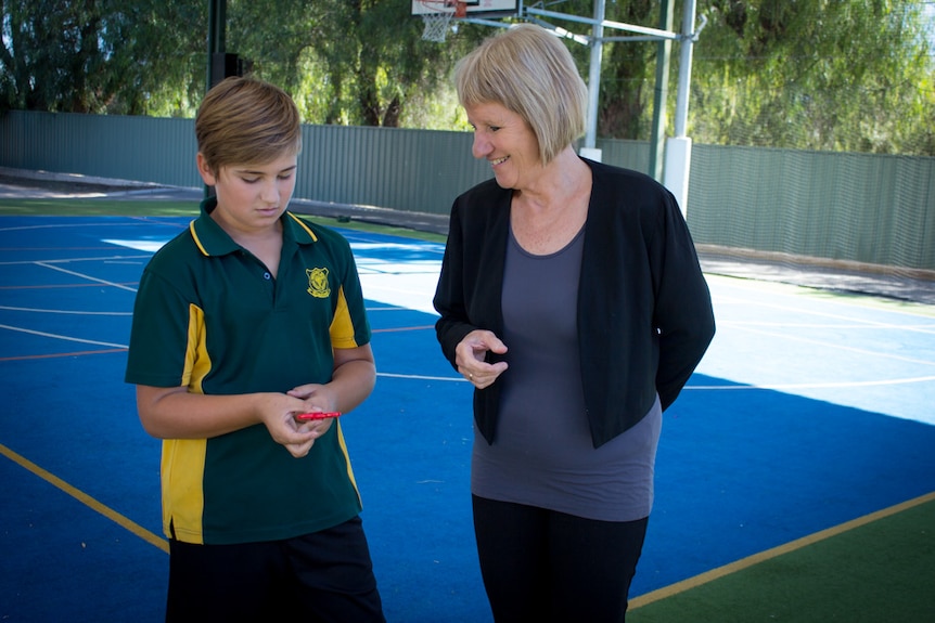 Judy Cottam and Will stand on a hardcourt looking at a fidget spinner toy in Will's hand.