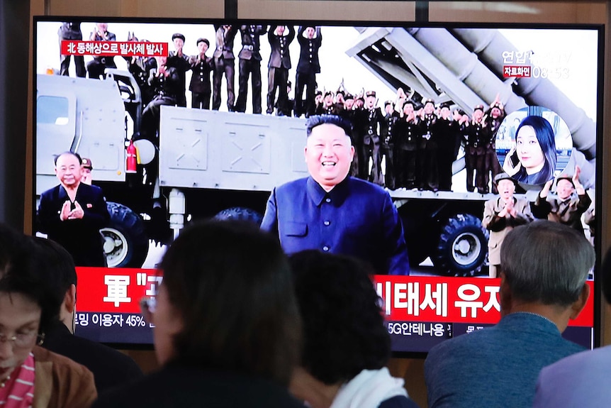 People gathered in front of television showing a smiling North Korean leader in front of a military truck with rocket launchers.