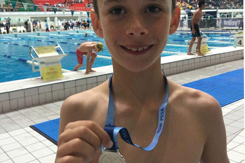 Boy holding his diving medal in front of the pool