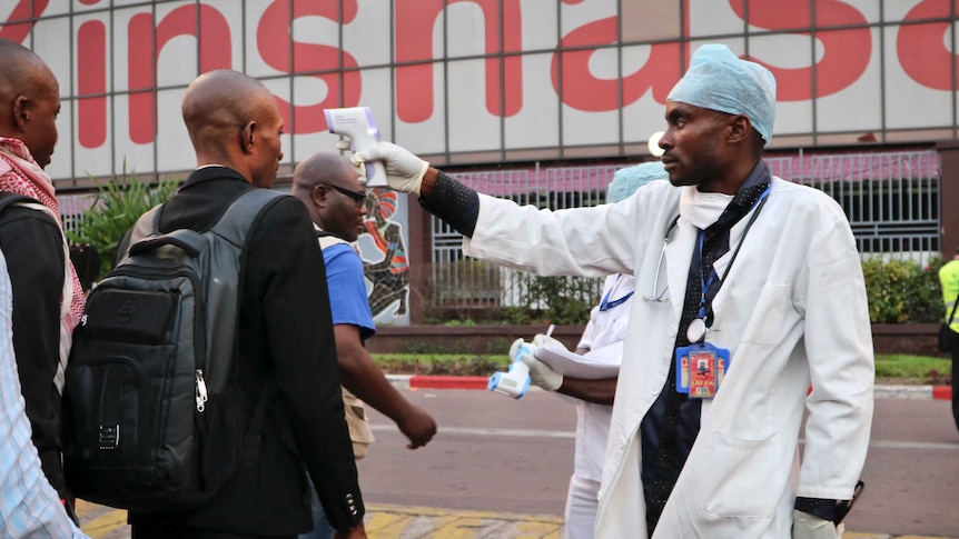 A health care worker checks the temperature of people as they walk through a line