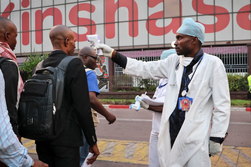 A health care worker checks the temperature of people as they walk through a line